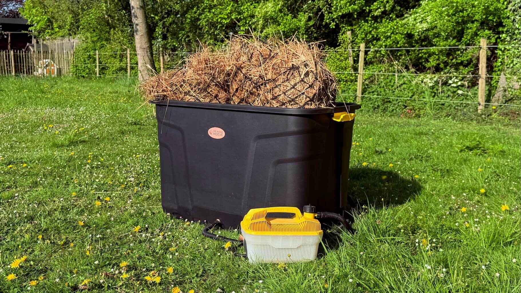 Hooistomer De Trog met hooi en stoomslang zichtbaar, opgesteld in de wei op het gras.