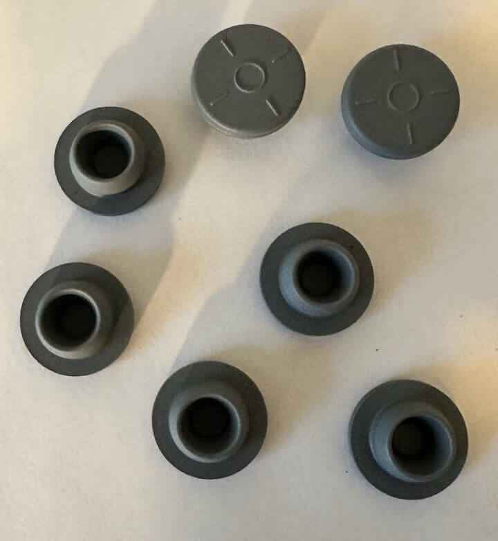 Zeven grijze ronde rubberen dopjes op witte achtergrond.
